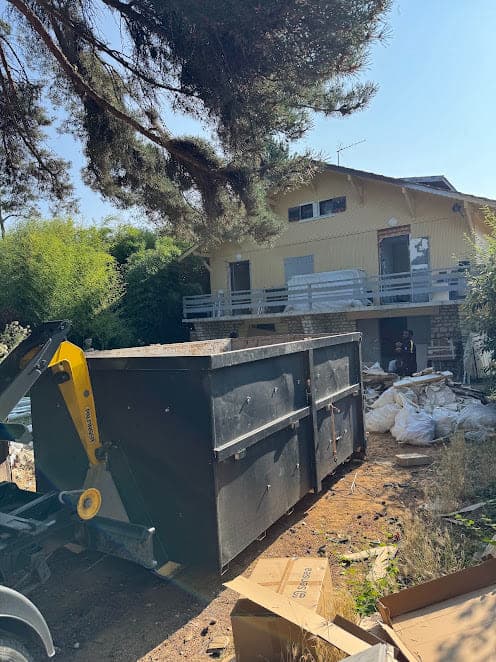 Benne noire livrée au camion-grue devant une maison individuelle en rénovation, big bags de gravats à côté